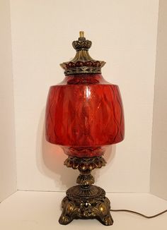 a red glass lamp sitting on top of a white table next to a light bulb