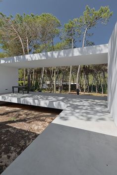 a white building with trees in the background and a bench on the ground near it