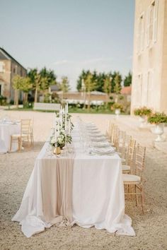 a long table is set up outside with white linens and flowers on the tables