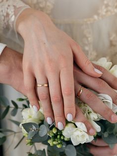 two people holding hands with wedding rings on their fingers and flowers in front of them