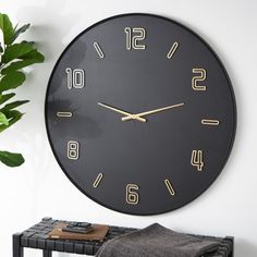 a black clock hanging on the wall next to a potted plant and towel rack