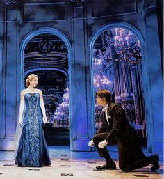 a man kneeling down next to a woman in a blue dress on top of a stage