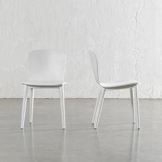 two white chairs sitting next to each other on a cement floor in front of a white wall