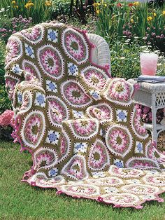 a crocheted blanket sitting on top of a lawn next to a chair and table