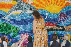 a woman standing in front of a group of children with bubbles on the wall behind her