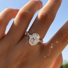 a woman's hand with a diamond ring on top of her finger and the sky in the background