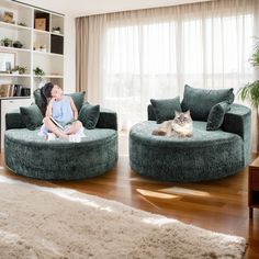 a woman sitting on a couch next to a cat in a living room with a large window