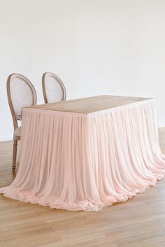 a table with two chairs and a pink cloth draped over it in front of a white wall