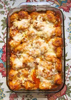 a casserole dish with meat and cheese in it on a floral table cloth