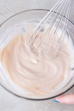 a whisk in a glass bowl filled with white sauce and other food ingredients