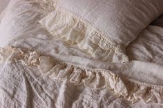 an unmade bed with white linens and ruffled pillows