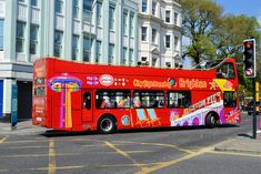 a red double decker bus driving down a street next to tall buildings and traffic lights