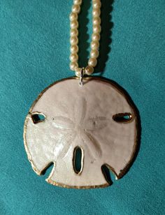 A beautiful sand dollar pendant. Hand painted gold with an opalescent enamel sealant. It is fragile but has been coated enough to keep it from breaking easily.  Walking on my favorite beach, I found this beauty and snatched it up as the prize it is. It will add an elegance to any outfit. White Pearl Pendant Jewelry For Beach, Ocean-inspired White Pearl Necklace Gift, White Medallion Pearl Necklace Gift, White Pearl Charm Medallion Necklace, White Medallion Necklace With Pearl Charm, Painted Sand Dollars, Sand Dollar Necklace, Sand Dollar Pendant, Necklace Diy