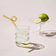 two glasses filled with water and limes next to each other on a white surface