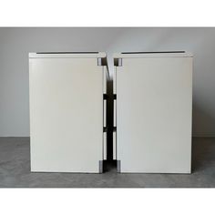 two white refrigerators sitting next to each other on top of a cement floor with doors open