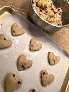 heart shaped cookies sitting on top of a cookie sheet next to a bowl of chocolate chips