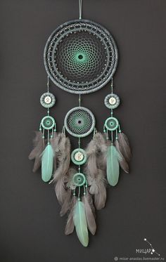 a dream catcher with feathers hanging from it's side on a gray wall next to a clock