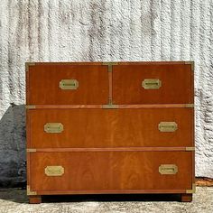 an old chest of drawers sitting on the ground next to a white wall with gold handles