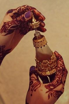 a person holding a bottle with henna tattoos on their arm and hand, while wearing a ring around the neck