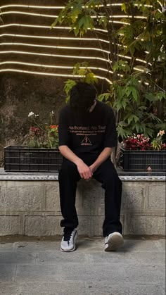 a person sitting on a ledge with their head down and his hands in his pockets