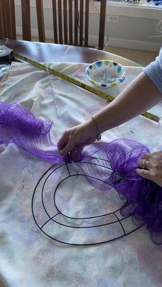 a woman is working on something with purple fabric and scissors at the table in front of her