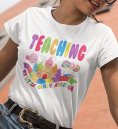 a woman wearing a white teaching shirt with candy kingdom on the front and rainbow writing on the back