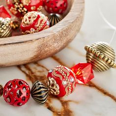 several red and gold colored beads on a marble surface next to a wooden bowl filled with other decorative objects