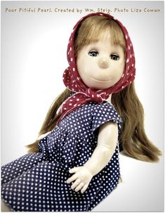 a doll with long hair wearing a red bandana and blue polka dot dress sitting on the ground