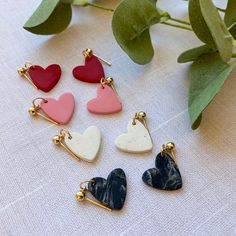 four heart shaped charms sitting on top of a table next to a plant with leaves