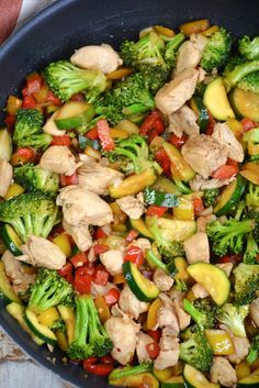 a skillet filled with chicken, broccoli and peppers