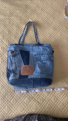 a blue jean purse sitting on top of a bed next to a tape measure ruler