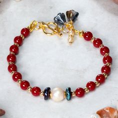 Beautiful Red coral, Pearl and gold plated Hematite bracelet designed and handcrafted with care and attention to detail. The bracelet is  hand threaded onto quality 19 strand beading wire for flexibility and durability using:     6mm dyed Red Coral beads,     Freshwater pearl focal bead,     2mm Gold plated Hematite beads,      Dark blue wavy Picasso Czech glass accent disc     beads.  The bracelet measures 19cm and is fastened using a quality 18ct gold plated toggle clasp which is adorned with Elegant Red Pearl Bracelets, Red Pearl Bracelets With Round Beads, Adjustable Red Jewelry With Pearl Charm, Red Pearl Bracelet As A Gift, Red Pearl Bracelet As Gift, Red Pearl Bracelet Gift, Elegant Red Handmade Charm Bracelet, Elegant Handmade Red Charm Bracelet, Red Pearl Beaded Bracelets As Gift