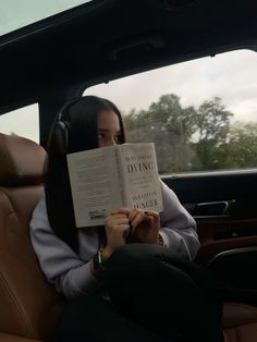 a woman sitting in the back seat of a car reading a book