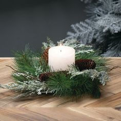 a lit candle sitting on top of a wooden table next to pine cones and evergreen branches