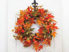 a wreath with orange and green leaves hanging on a door