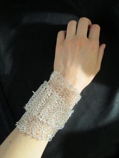 a woman's hand wearing a white lace bracelet on top of a black surface