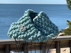 a blue knitted bag sitting on top of a wooden fence next to the ocean