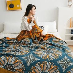 a woman sitting on top of a bed covered in a blue and orange comforter