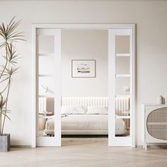 a bedroom with white walls and wooden flooring next to a large potted plant