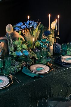 the table is set with blue and green plates, silverware, flowers and candles