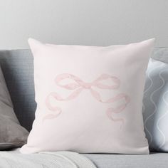 a white pillow with pink ribbon on it sitting on a couch next to pillows and throw pillows