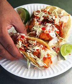 two fish tacos on a paper plate with lime wedges