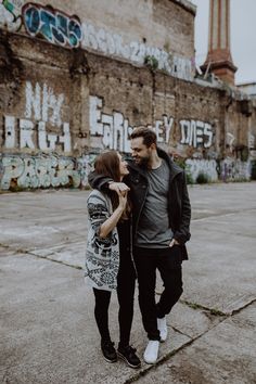 a man and woman standing next to each other in front of graffiti covered wall with buildings