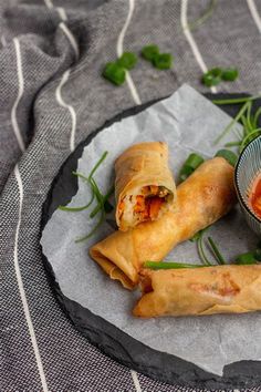 two vegetable spring rolls on a plate with dipping sauce in a small bowl next to them