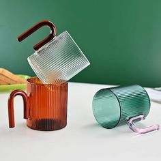 three different colored glass cups sitting on top of a white table next to each other