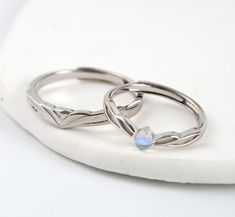 two silver rings sitting on top of a white plate with an opal stone in the middle