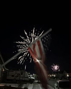 an american flag is blowing in the wind on a street at night with fireworks behind it