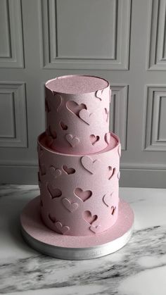 three tiered pink cake with hearts cut out of the side on a marble table