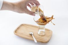 a person pouring something into a glass on top of a wooden tray with utensils