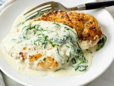 a white plate topped with chicken covered in gravy and spinach on top of mashed potatoes